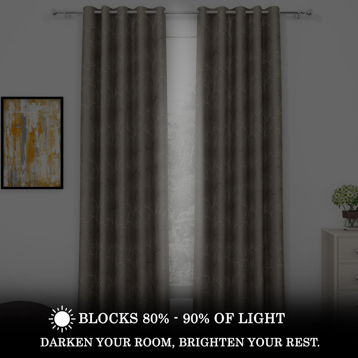 Two blackout curtains in dark gray with ivory and copper branch patterns, hanging on a silver rod, blocking 80%-90% light