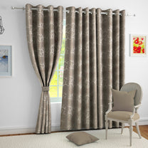 Two blackout curtains in taupe with ivory and copper branch foil print, hanging on a silver rod in a living room setting