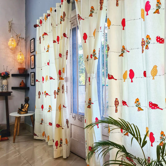 Bright room with colorful bird-patterned curtains, a small plant, wall art, and decorative lanterns nearby.