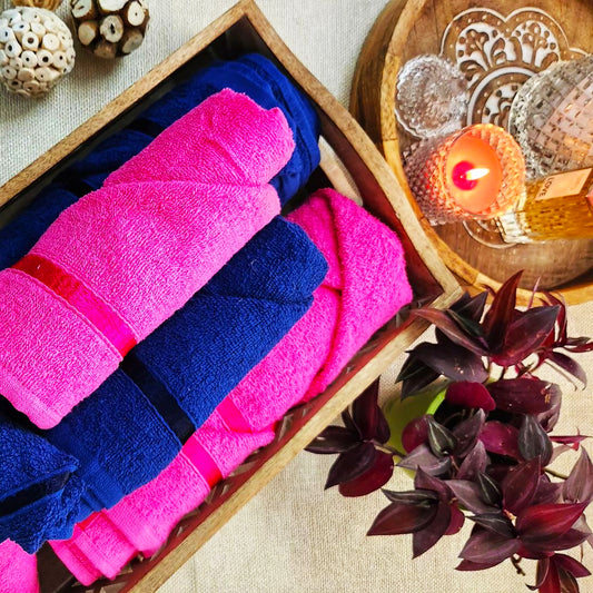  A wooden tray with neatly rolled pink and blue towels, a lit candle, and a small plant beside it.